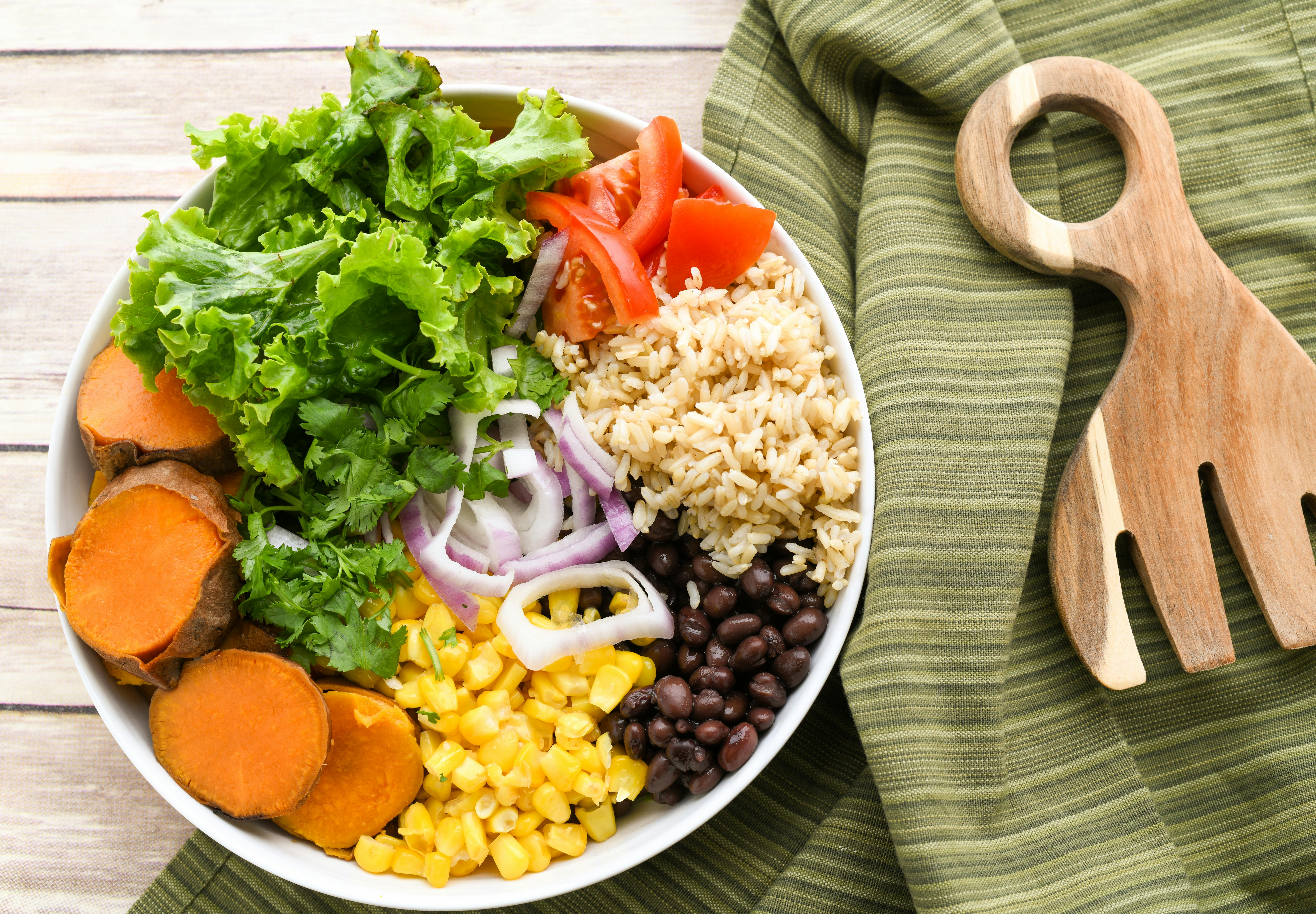 Healthy buddha bowl with fresh vegetables, rice, and beans on a wooden table.